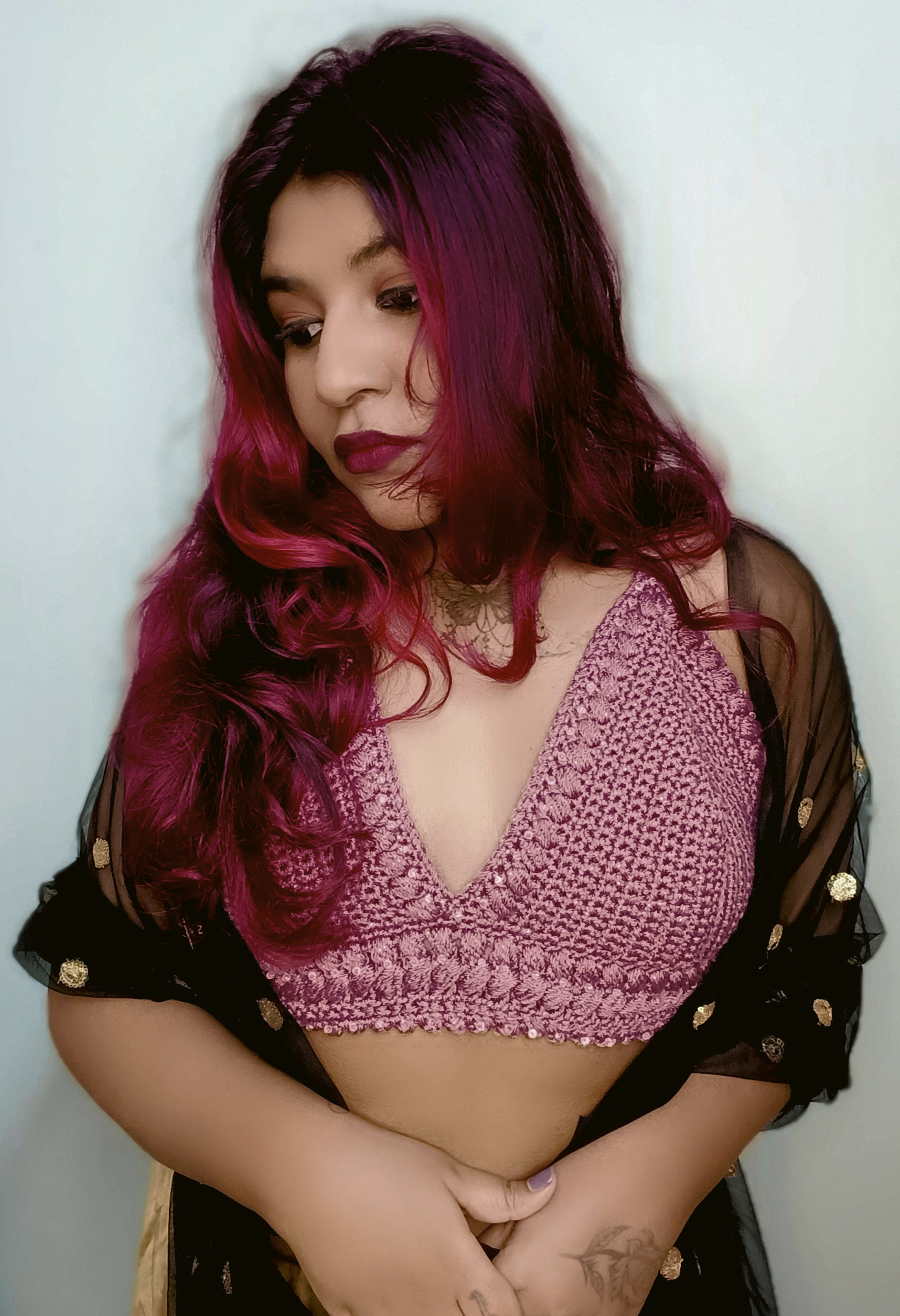 Person wearing a dusty pink crochet top with a black sheer cover-up against a white background