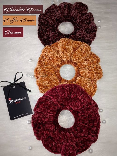 Three crocheted velvet hair scrunchies in chocolate brown, coffee brown, and maroon with a brand tag on a light background.