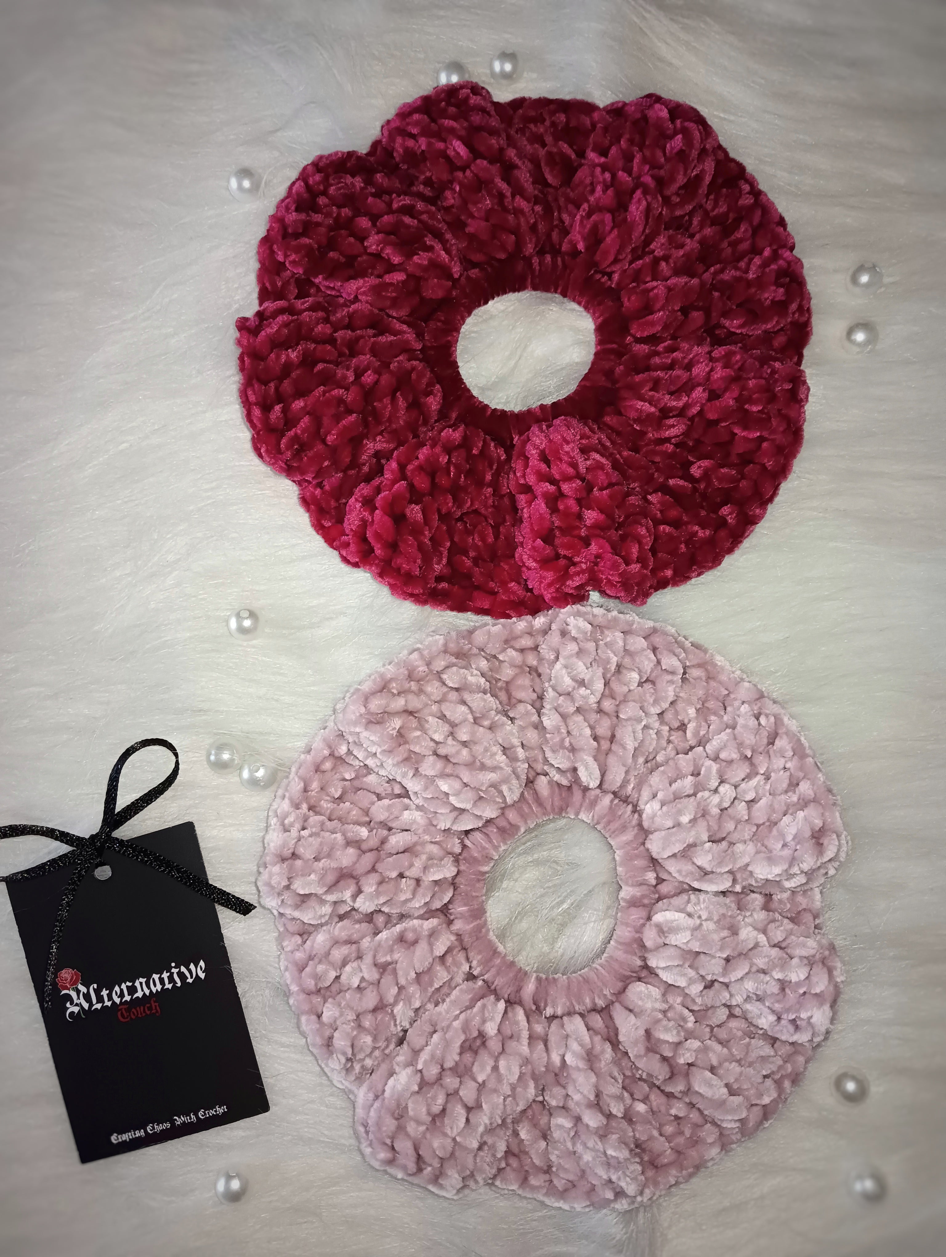 Two crochet velvet scrunchies on a light surface with a brand tag.