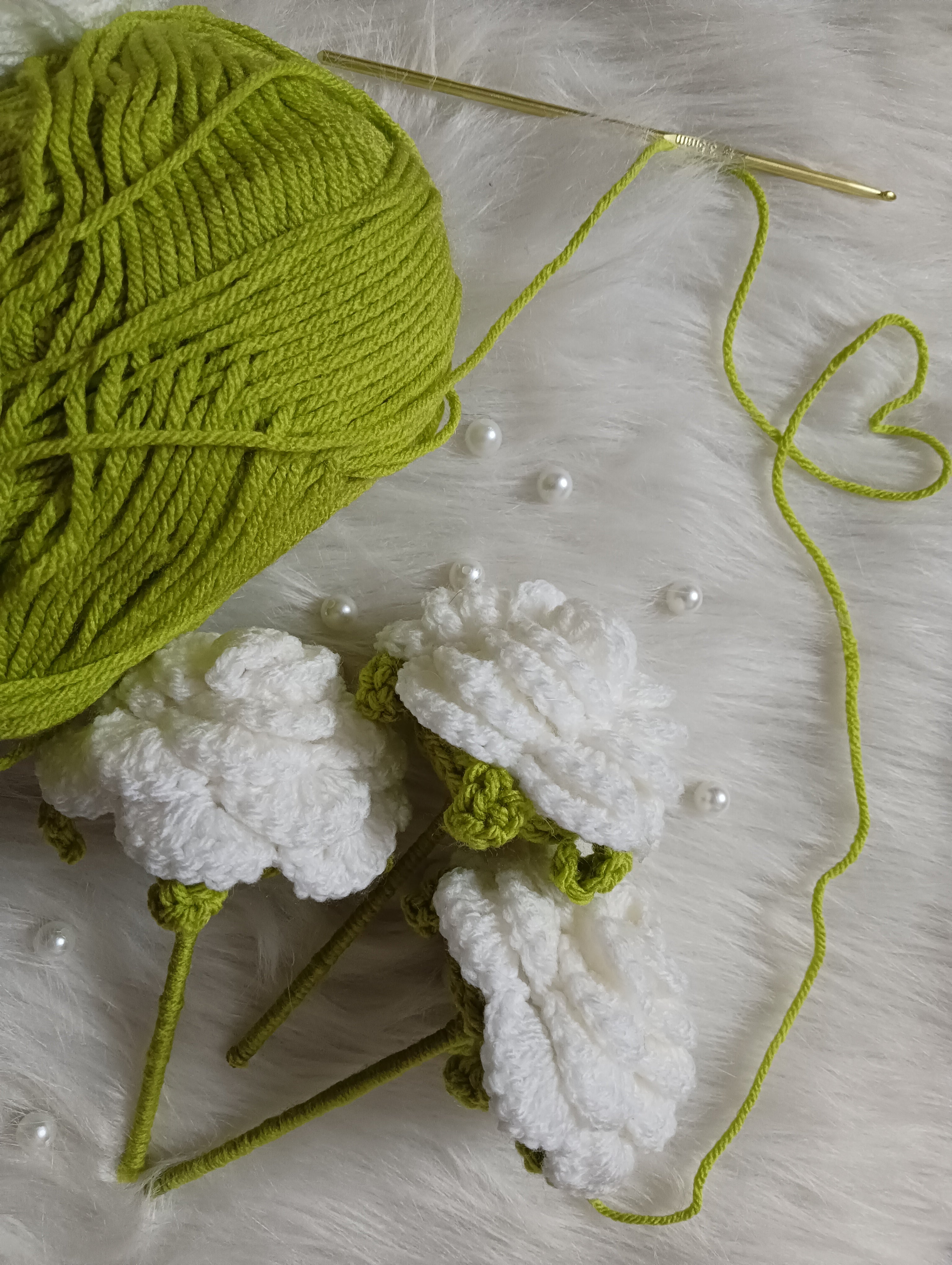 Green yarn ball with white crocheted roses on a textured surface