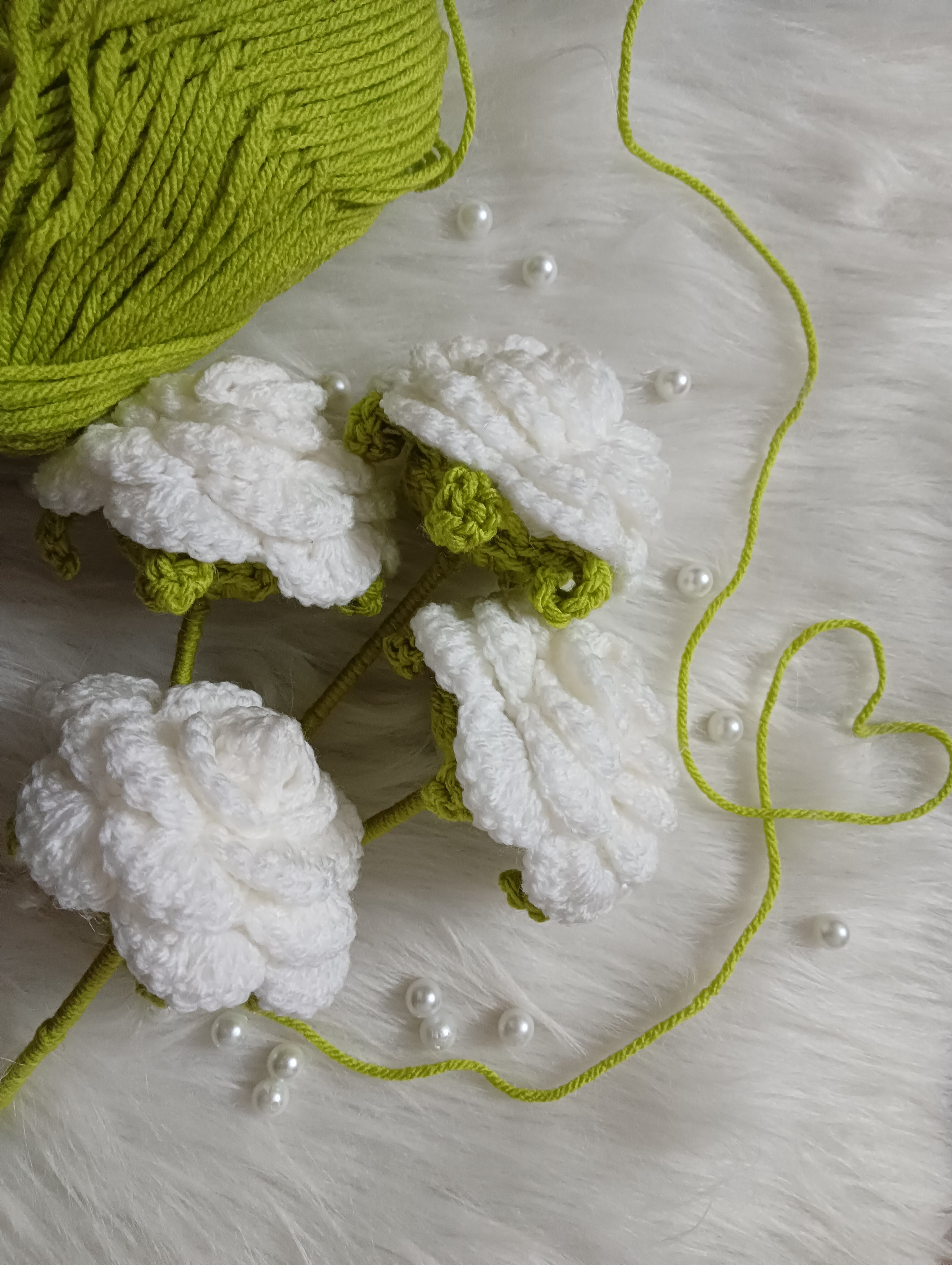 White crocheted roses with green yarn on a textured white surface