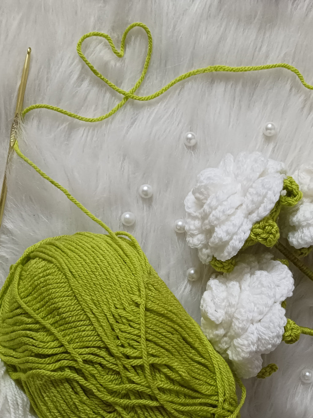 Green yarn ball with crochet hook and crocheted white roses on a light textured surface.