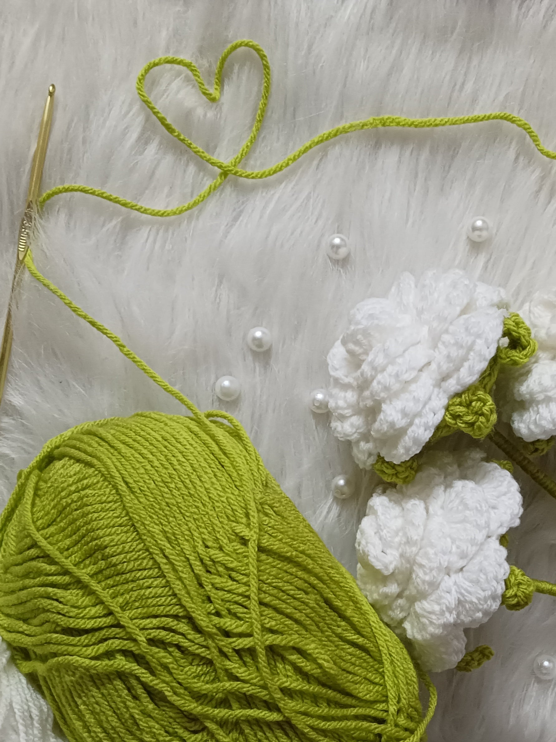 Green yarn ball with crochet hook and crocheted white roses on a light textured surface.