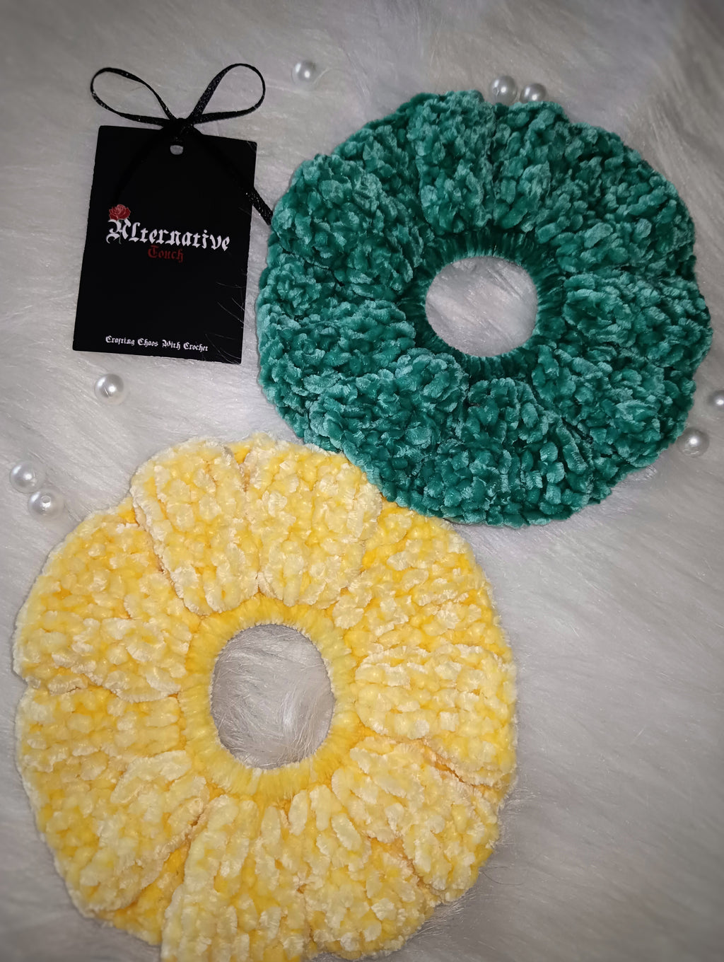 Two scrunchies, one peacock green and one light yellow, with a brand tag on a light surface.