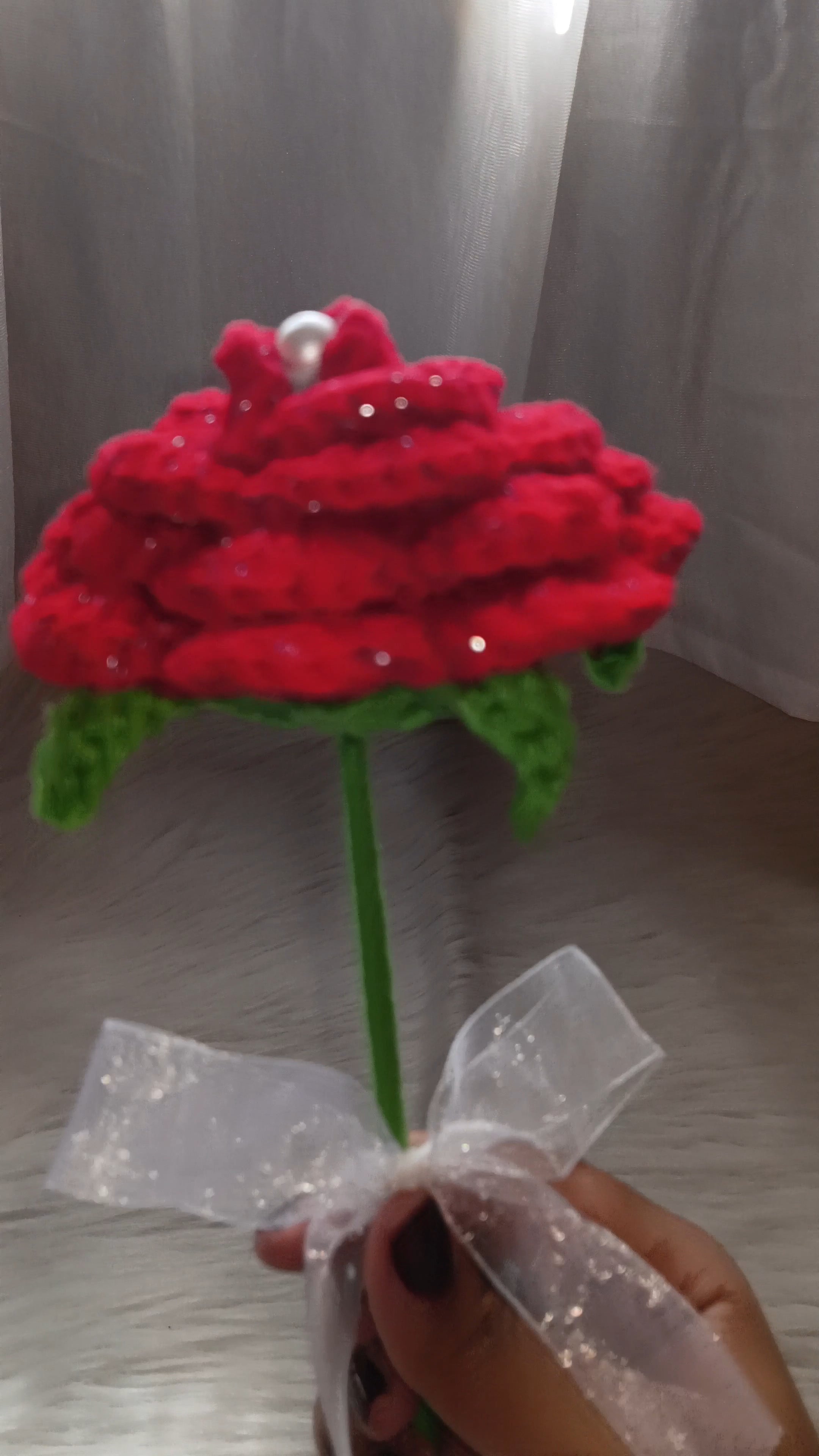 Red shimmering rose with a pearl in the center and a white bow on the green stem.